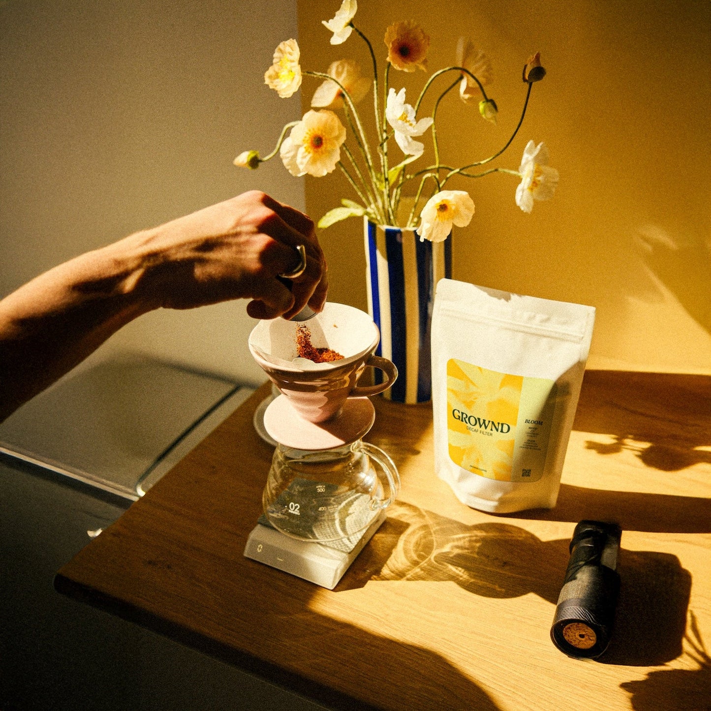 Person making coffee using a pour-over method with a bag of 'CROWND' coffee on a wooden table.